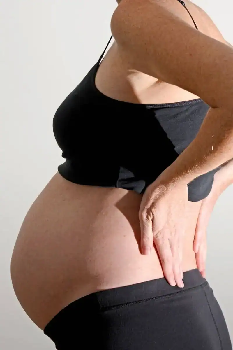 Pregnant woman gently holding her lower back, symbolising relief from pregnancy-related discomfort through acupuncture support.